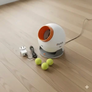 The iFetch ball launcher unit, three mini tennis balls, and a UK mains power adapter laid out on a wooden floor.