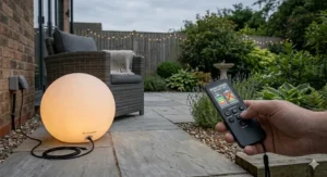 A hand holding a remote control to change the colour of a rechargeable glow ball, featuring British English spelling for colour.