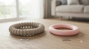 An educational infographic comparing two products on a wooden surface: the firm, beige-grey rubber ring on the left labeled "FIRM" and a softer, smooth pink ring on the right labeled "SOFT".